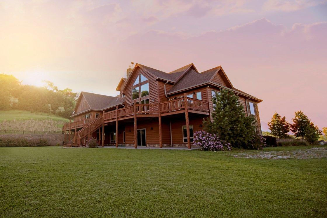 A log-sided home with a wraparound deck and walkout lower level on a well-kept lawn at sunset.